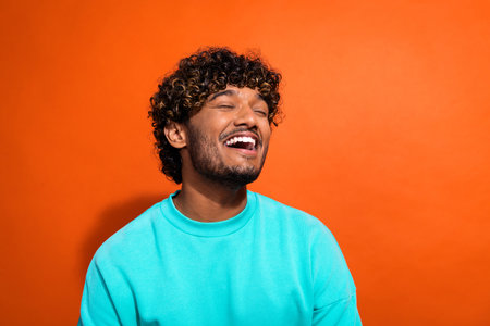 Photo of carefree overjoyed person closed eyes toothy smile good mood laughing isolated on orange...