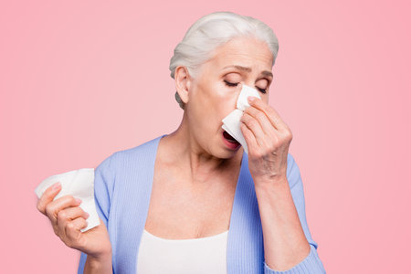 Grey haired old beautiful caucasian woman wearing casual suffering from fever, coughing, sneezing. Isolated over violet pastel backgroundの写真素材