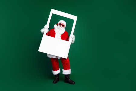 Full length photo of positive good mood santa dressed red costume taking new year photo empty space isolated green color backgroundの写真素材