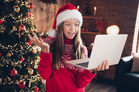 Photo of sweet charming small girl wear red print sweater getting modern gadget new year xmas greetings indoors house roomの写真素材