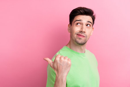 Photo of young thoughtful pensive man dressed green t shirt point finger empty space creative idea isolated on pink color backgroundの写真素材