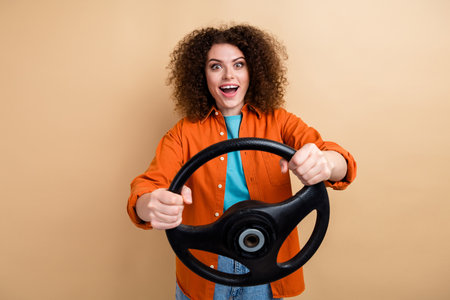 Photo of cheerful lovely girl wear trendy orange clothes hands hold steering wheel test drive lesson isolated on beige color backgroundの写真素材