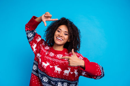 Photo of cheerful popular blogger young girl showing fingers portrait cadre shooting her toothy smile isolated on blue color backgroundの写真素材