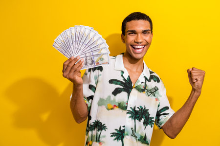 Photo of ecstatic overjoyed man with nose piercing wear print shirt holding bunch of dollars win bet isolated on yellow color backgroundの写真素材