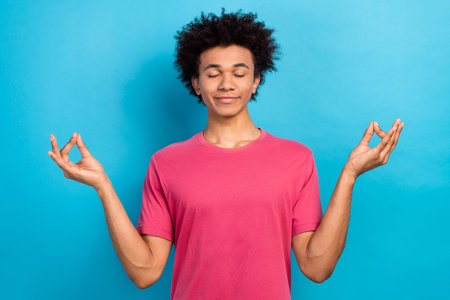 Photo of calm peaceful guy wear pink stylish clothes hands showing om symbol isolated on blue color backgroundの写真素材