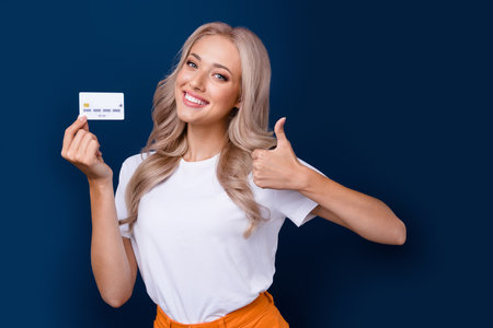 Photo of charming girl wear stylish clothes recommend cashless payment thumb up empy space isolated on dark blue color backgroundの写真素材