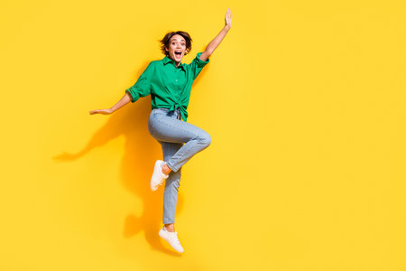 Full length photo of cheerful pretty lady wear green shirt jumping high having fun empty space isolated yellow color backgroundの写真素材