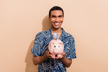 Photo portrait of nice young male hold pig banking banknote insert wear trendy blue print garment isolated on beige color backgroundの写真素材