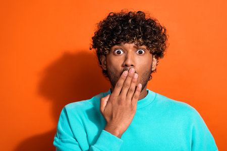 Portrait of impressed terrified person arm covering mouth staring empty space isolated on orange color backgroundの写真素材