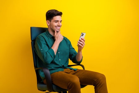 Photo of handsome attractive man dressed stylish clothes sitting armchair talking online reading news isolated on yellow color backgroundの写真素材
