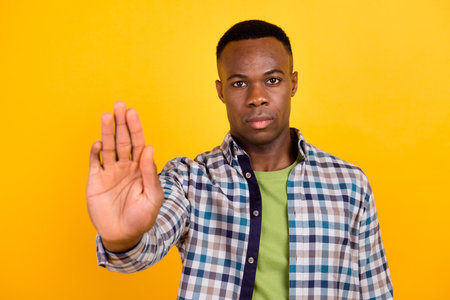 Photo of young concentrated worker guy wear plaid shirt demonstrate stop enough discrimination isolated on yellow color backgroundの写真素材