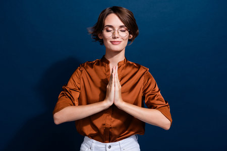 Photo portrait of lovely young lady show pray gesture meditate wear trendy brown blouse isolated on dark blue color backgroundの写真素材