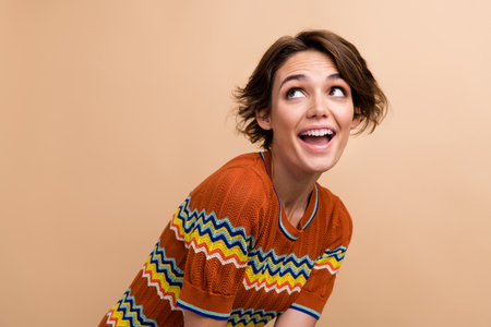Portrait of astonished cheerful girl open mouth look interested empty space isolated on beige color...