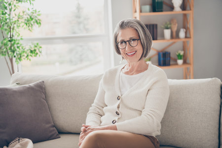 Photo of gorgeous cheerful lady sitting on couch wearing stylish sweater spending weekend at home...