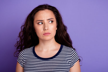 Portrait of young suspicious woman with curly brunette hair dressed striped t shirt thinking ponder isolated on purple color backgroundの写真素材