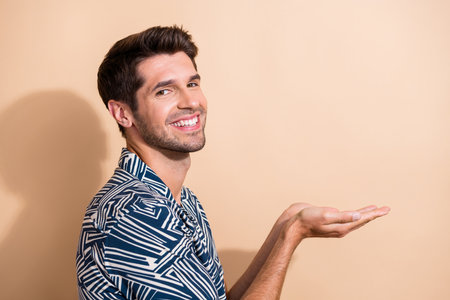 Profile side photo of nice handsome man dressed trendy clothes presenting haircare product empty space isolated on beige color backgroundの写真素材