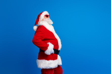 Photo portrait of retired old man touch belt shopping promo wear trendy santa claus costume coat isolated on blue color backgroundの写真素材