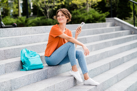 Photo of cheerful thoughtful lady wear orange t-shirt spectacles typing on a laptop outside urban...