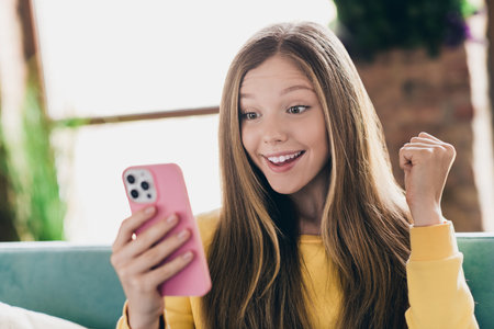 Photo of optimistic ecstatic overjoyed girl with straight hairdo dressed yellow pullover read message on smartphone inside indoorsの写真素材