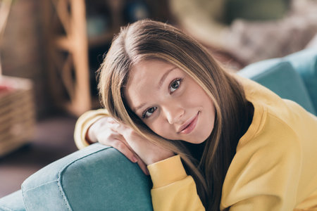 Close up portrait of cute peaceful schoolgirl teenager lying on corner couch relaxed chilling at home isolated blurred apartment backgroundの写真素材