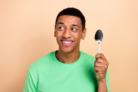 Photo portrait of attractive young man hold spoon look empty space wear trendy green clothes isolated on beige color backgroundの写真素材