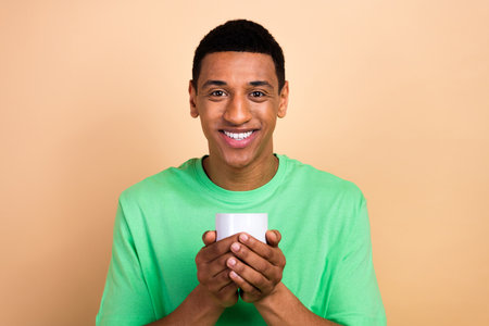 Photo portrait of nice young male hold white coffee cup cafe wear trendy green outfit isolated on beige color backgroundの写真素材