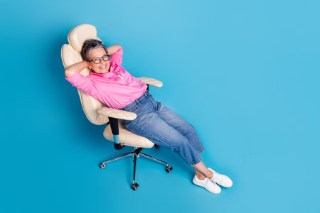 Full size photo of good mood funny woman dressed pink shirt in glasses lay on chair arms behind head isolated on blue color backgroundの写真素材