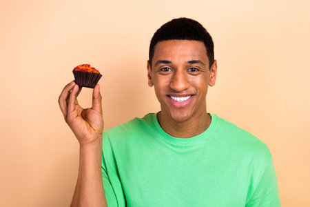 Photo portrait of attractive young man hold muffin sweet dessert food wear trendy green clothes isolated on beige color backgroundの写真素材