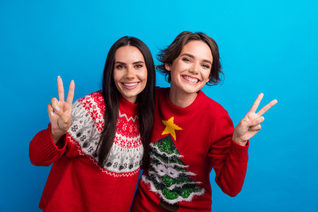 Photo of positive girls making v sign on christmas party isolated blue color background