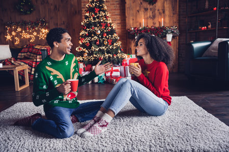 Full size portrait of two funny positive people sit carpet floor drink hot chocolate speak new year tree lights indoorsの写真素材
