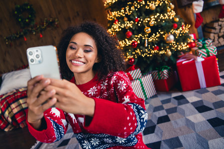 Photo of charming cute girl sitting on fluffy carpet in comfort room talking with family rejoicing magic winter time tree garlands indoorsの写真素材