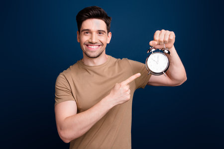 Photo of successful attractive man wear stylish beige clothes demonstrate clock watch time for work isolated on dark blue color backgroundの写真素材