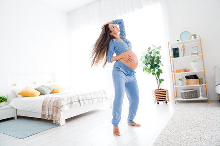 Photo of overjoyed glad cute pregnant girl with big tummy good mood free carefree time white interior indoorsの写真素材