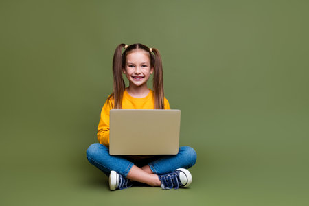 Full size photo of smart clever optimistic small kid wear yellow pullover doing homework on laptop isolated on khaki color backgroundの写真素材