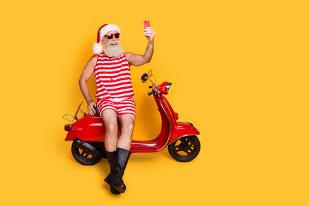 Full length photo of funky senior guy christmas swimwear hat recording video delivering gifts empty space isolated yellow color backgroundの写真素材