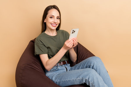 Portrait of adorable starting career blogger mom mature woman hold smartphone and chill sit bean bag isolated on beige color backgroundの写真素材