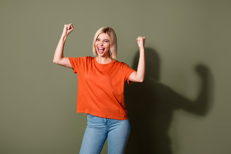 Photo portrait of lovely young lady raise fists winning celebrate dressed stylish orange garment isolated on khaki color backgroundの写真素材