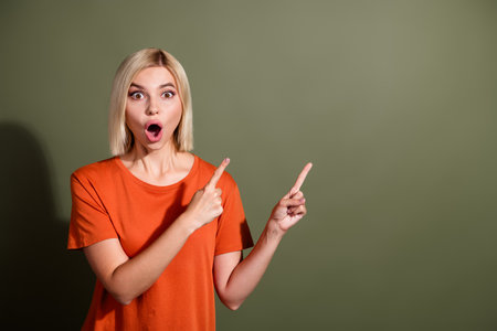 Photo portrait of lovely young lady point empty space shocked open mouth dressed stylish orange garment isolated on khaki color backgroundの写真素材