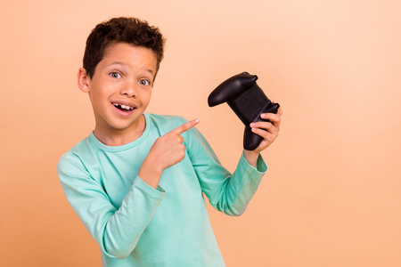 Photo of glad cheerful boy wear trendy turquoise clothes recommend buy a game controller isolated on...