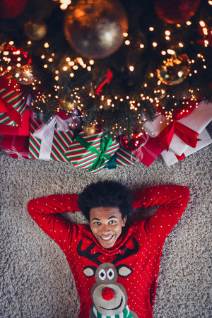 Top view photo of funky carefree guy wear red ugly xmas sweater relaxing arms behind head enjoying christmas indoors apartment roomの写真素材