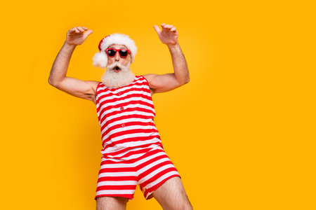 Photo of cool cheerful elderly guy wear new year swimsuit hat sunglass enjoying disco empty space isolated yellow color backgroundの写真素材