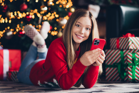 Portrait of smiling young teenager smiling girl with new apple smartphone browsing wish list for christmas holly jolly at home indoorsの写真素材
