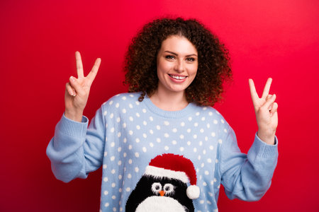 Portrait of cheerful positive young funny lady wear penguin print jumper gesture double symbol v sign isolated on red color backgroundの写真素材