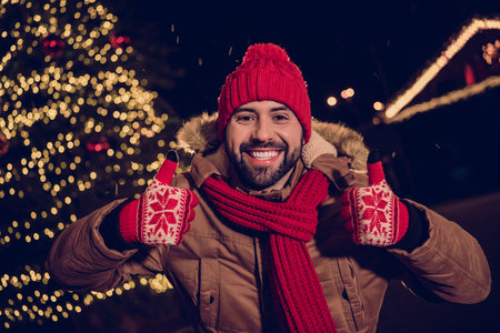 Photo of cheerful confident guy dressed coats showing thumbs up enjoying x-mas time outdoors urban fair parkの写真素材