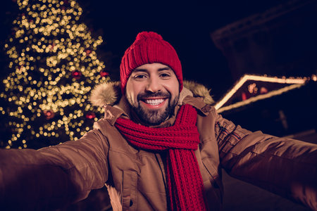 Photo of dreamy cheerful young guy dressed coat recording video x-mas vlog outdoors urban fair parkの写真素材