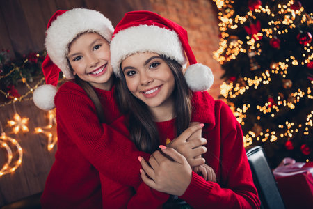 Photo of excited good mood little siblings dressed ugly print christmas sweaters cuddling embracing indoors house roomの写真素材