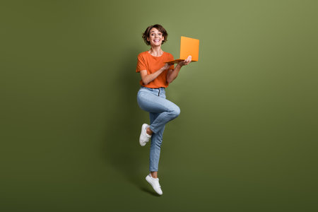 Full size photo of impressed excited woman dressed orange shirt hold laptop jumping find sale in...