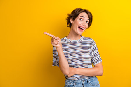 Portrait of impressed girl with short hairdo wear grey t-shirt directing look at discount empty space isolated on yellow color backgroundの写真素材