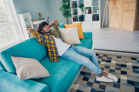 Full length photo of positive nice man sit couch closed eyes hands behind head inspiration recreation house insideの写真素材