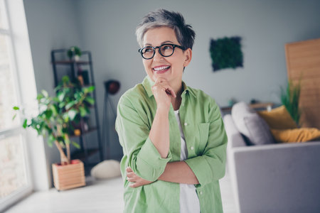 Photo of thoughtful businesswoman wearing khaki shirt touch chin thinking planning looking novelty window side fantasizing ideas indoorsの写真素材